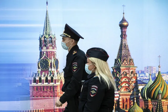 Police officers wearing face masks to protect against coronavirus walk past a photo of Kremlin's Spasskaya Tower, left, and St. Basil's Cathedral in Sheremetyevo Airport, outside Moscow, Russia, Friday, October 9, 2020. The coronavirus outbreak in Russia continues its rapid growth. (Photo by Pavel Golovkin/AP Photo)