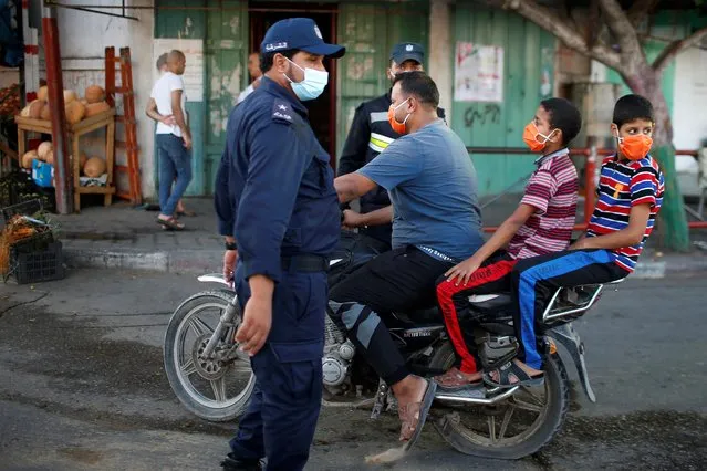 A Palestinian man with his children wearing protective face masks rides his motorcycle by police officers amid the coronavirus disease (COVID-19) outbreak, in the northern Gaza Strip on September 22, 2020. (Photo by Suhaib Salem/Reuters)