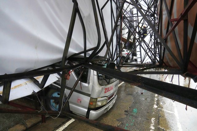 A rescue worker climbs a toppled billboard that damaged a parked truck in Quezon city, Philippines due to enhanced winds and rain as Tropical Storm Wipha, locally called Crising, exits the northern portion of country on Saturday, July 19, 2025. (Photo by Aaron Favila/AP Photo)