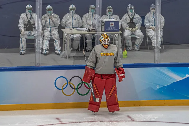 A goalkeeper of China's ice hockey national team for the Winter Olympics attends a training session as behind sit medical workers wearing protective gear, at the National Indoor Stadium, in Beijing, China, 31 January 2022. The Beijing 2022 Winter Olympics is scheduled to start on 04 February 2022. (Photo by Roman Pilipey/EPA/EFE)