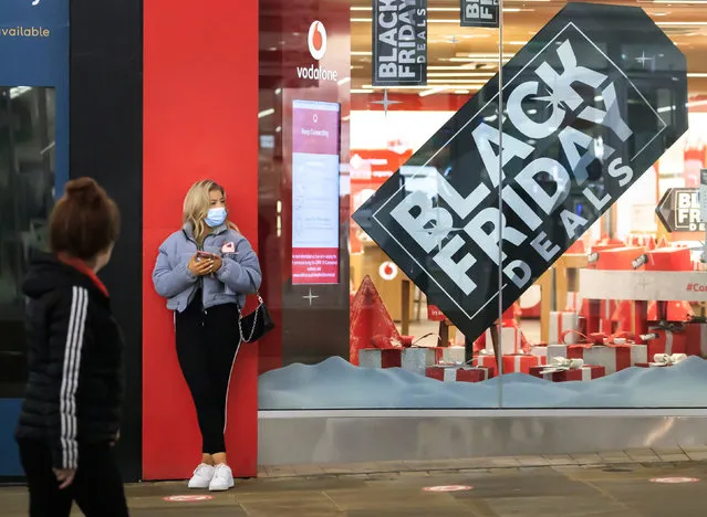 A woman next to a Black Friday poster in the window of a mobile phone store in Manchester city centre, England, although most stores remain closed Saturday November 28, 2020. A four-week national lockdown to curb the spread of coronavirus is still restricting civil liberties and will put more pressure on shops to attract customers back to shopping streets when restrictions are relaxed in the run-up to Christmas. (Photo by Danny Lawson/PA Wire via AP Photo)