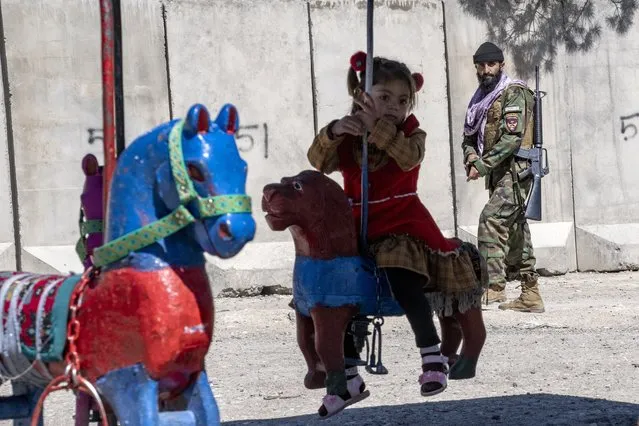 A Taliban fighter stands guard on Nadir Khan hill while a girl rides a merry-go-round, during the first day of Eid al-Fitr in Kabul, Afghanistan, Friday, April 21, 2023. (Photo by Ebrahim Noroozi/AP Photo)