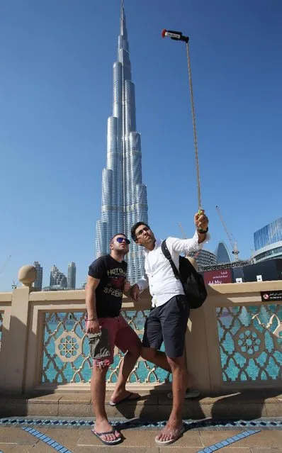 In this Tuesday, January 6, 2015 photo, Rasul Alekberov holds a selfie stick next to his friend Gudrat Aghayev both tourists from Republic of Azerbaijan while they take a selfie in front of “Burj Khalifa”, world's tallest tower in Dubai, United Arab Emirates. (Photo by Kamran Jebreili/AP Photo)