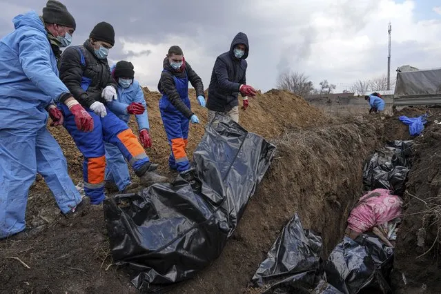 Dead bodies are placed into a mass grave on the outskirts of Mariupol, Ukraine, Wednesday, March 9, 2022, as people cannot bury their dead because of the heavy shelling by Russian forces. (Photo by Evgeniy Maloletka/AP Photo)