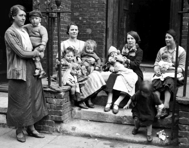 Mothers with their children in front of their tenement homes, in Limehouse, London, on May 17, 1928. (Photo by AP Photo)