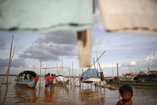 Ethnic Cham Muslim children pass the time by their boats on the banks of Mekong river in Phnom Penh July 27, 2013. About 100 ethnic Cham families, made up of nomads and fishermen without houses or land who arrived at the Cambodian capital in search of better lives, live on their small boats on a peninsula where the Mekong and Tonle Sap rivers meet, just opposite the city's centre. The community has been forced to move several times from their locations in Phnom Penh as the land becomes more valuable. They fear that their current home, just behind a new luxurious hotel under construction at the Chroy Changva district is only temporary and that they would have to move again soon. (Photo by Damir Sagolj/Reuters)