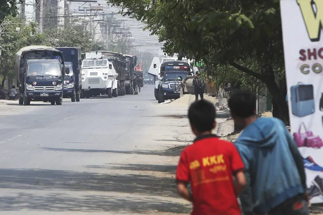 People watch as a row of vehicles by security forces are parked on a road in Mandalay, Myanmar Friday, March 19, 2021. The authorities in Myanmar have arrested a spokesman for ousted leader Aung San Suu Kyi's political party as efforts to restrict information about protests against last month's military takeover are tightened. (Photo by AP Photo/Stringer)