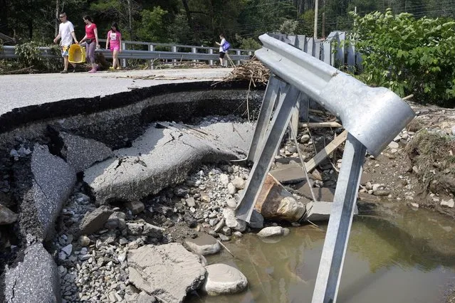 People walk across a bridge damaged by flood waters, Tuesday, July 11, 2023, in Ludlow, Vt. A storm that dumped two months of rain in two days caused erosion along many roadways in the state. (Photo by Steven Senne/AP Photo)
