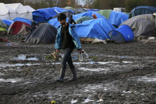 A migrant holds running shoes as he walks in a muddy field called the Grande-Synthe jungle, a camp of makeshift shelters where migrants and asylum seekers from Iraq, Kurdistan and Syria gather in Grande-Synthe, France, December 30, 2015. (Photo by Pascal Rossignol/Reuters)
