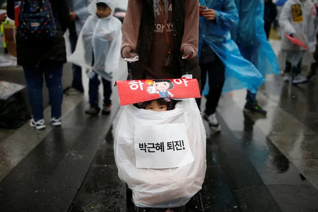 A woman pushes her daughter on a stroller during a protest calling for Park Geun-hye to step down as it snows in central Seoul, South Korea, November 26, 2016. The sign on a stroller reads “Step down Park Geun-hye”. (Photo by Kim Kyung-Hoon/Reuters)
