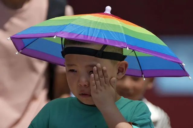 A boy wearing a rainbow umbrella wipes his sweat as he visits the Forbidden City on a sweltering day in Beijing, Friday, July 7, 2023. Earth's average temperature set a new unofficial record high on Thursday, the third such milestone in a week that already rated as the hottest on record. (Photo by Andy Wong/AP Photo)