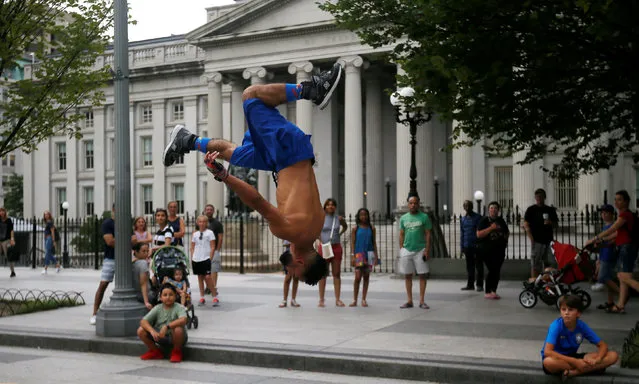 A street performer flips through the air in front of the U.S. Treasury building as tourists and passersby look on in Washington, U.S., August 17, 2018. (Photo by Jim Bourg/Reuters)