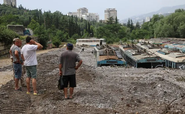 Residents look at the aftermath of flood on a trolleybus parking after heavy rainfall in Yalta, Crimea on June 22, 2021. (Photo by Alexey Pavlishak/Reuters)