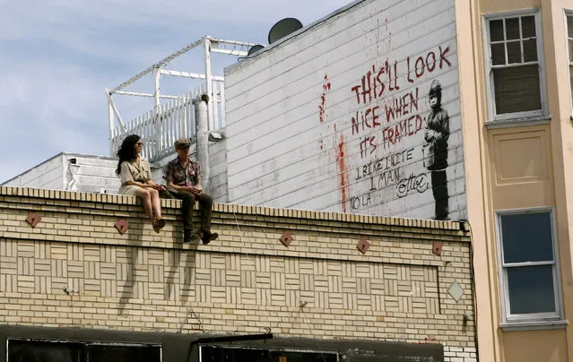 A couple sits on a rooftop featuring a painting, believed to be the work of elusive British street artist Banksy, in the Mission District of San Francisco, May 4, 2010. (Photo by Robert Galbraith/Reuters)