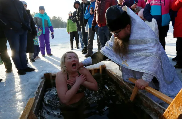 Priest Sergei Ryzhov conducts a ceremony as a woman takes a dip in the freezing waters of Lake Buzim during celebrations of the Orthodox Christian feast of Epiphany north of Krasnoyarsk, Russia on January 19, 2019. (Photo by Ilya Naymushin/Reuters)