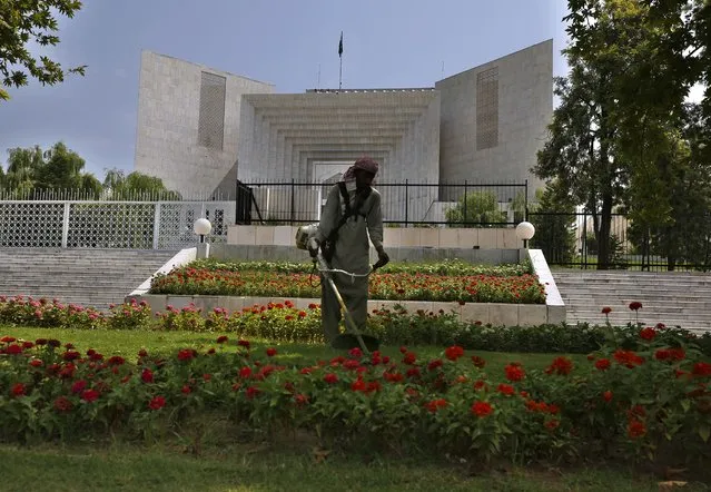 A worker mows the front lawn of the Supreme Court building where the hearing of the Hindu temple attack case is held in Islamabad, Pakistan, Friday, August 6, 2021. A Muslim mob stormed a Hindu temple in a remote town in Pakistan's eastern Punjab province on Wednesday, damaging statues and burning down the temple's main door. The attack followed an alleged desecration of a madrassa, or religious school, by a Hindu boy earlier this week, police said. (Photo by Anjum Naveed/AP Photo)