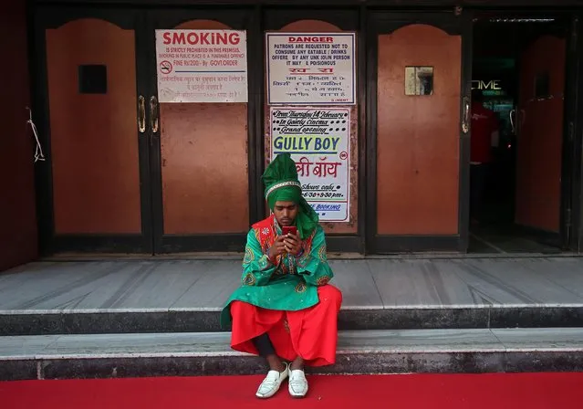 A man wearing traditional attire checks his mobile phone as he waits to perform before the launch of the trailer of a Bollywood movie outside a cinema in Mumbai, February 20, 2019. (Photo by Francis Mascarenhas/Reuters)