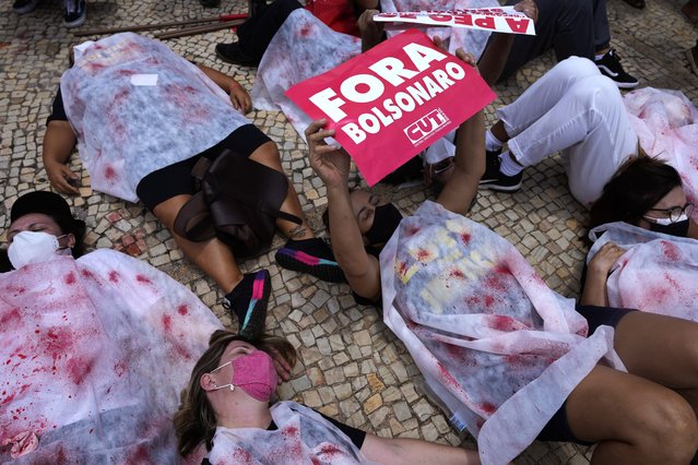 Demonstrators are dressed in sheets covered by fake blood to represent people who died of COVID-19, one holding the Portuguese message “Get out Bolsonaro”, referring to the president, outside the Planalto presidential palace, in Brasilia, Brazil, Wednesday, October 20, 2021. (Photo by Eraldo Peres/AP Photo)