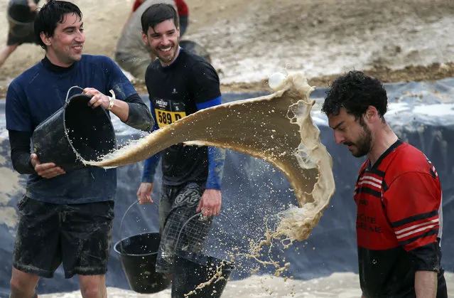 A participant in the Mud Day event throws a bucket of mud at a friend during the Mud Day run in Beynes, west of Paris, Thursday, May 8, 2014. Thousands of runners seeking a challenge competed in a circuit of approximately 13 kilometers (8 miles) with over 20 obstacles, most of them set in mud. (Photo by Francois Mori/AP Photo)