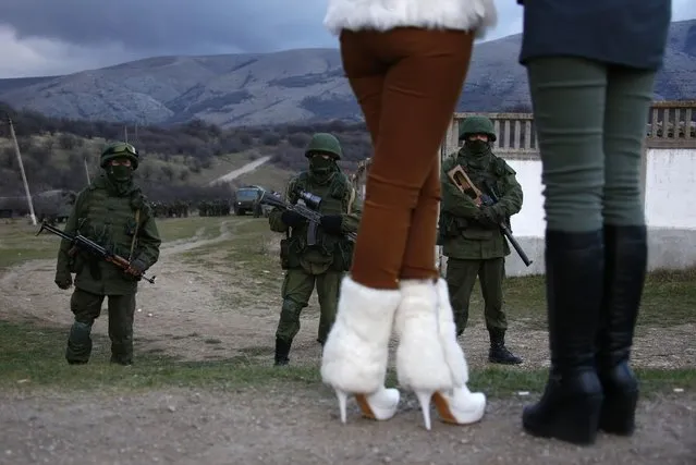 Local women watch armed men, believed to be Russian soldiers, assemble near a Ukrainian military base in Perevalnoe March 5, 2014. (Photo by Thomas Peter/Reuters)