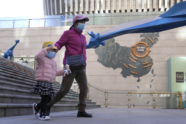 Residents wearing masks pass by a sign depicting Evergrande Group's China operation at a one of their commercial projects in Beijing, China, Tuesday, December 7, 2021. Evergrande Group's struggle to turn assets into cash has prompted fear a default might chill Chinese lending markets and cause global shockwaves. Economists say the ruling Communist Party can prevent a credit crunch but it wants to avoid sending the wrong signal by bailing out Evergrande in the middle of a campaign to force companies to cut debt Beijing worries is dangerously high. (Photo by Ng Han Guan/AP Photo)