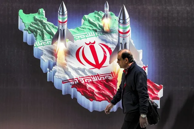 A man walks past a banner depicting missiles launching from a representation of the map of Iran coloured with the Iranian flag in central Tehran on April 15, 2024. Iran on April 14 urged Israel not to retaliate militarily to an unprecedented attack overnight, which Tehran presented as a justified response to a deadly strike on its consulate building in Damascus. (Photo by Atta Kenare/AFP Photo)