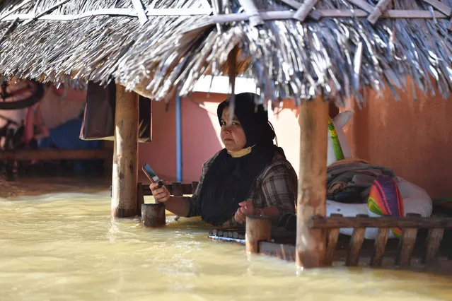 A Muslim woman sits holding her phone in floodwaters following heavy rains in the Muno Market in Sungai Kolok district, in the southern Thai province of Narathiwat on December 20, 2021. (Photo by Madaree Tohlala/AFP Photo)
