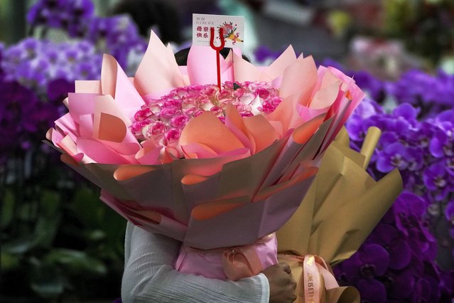 A woman carries a bouquet of roses with a greeting card that reads “Happy Mother's Day” bought from a flower wholesale market in Beijing, Sunday, May 12, 2024. (Photo by Andy Wong/AP Photo)