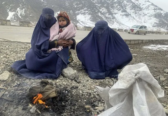 Gulnaz, left, keep her 18-month-old son warm themselves as they wait for alms in the Kabul – Pul-e-Alam highway eastern Afghanistan, Tuesday, January 18, 2022. The Taliban's sweep to power in Afghanistan in August drove billions of dollars in international assistance out of the country and sent an already dirt-poor poor nation, ravaged by war, drought and floods, spiralling toward a humanitarian catastrophe. (Photo by Kathy Gannon/AP Photo)