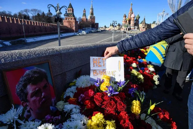 A man places a note reading “No to war!” among flowers at the site where late opposition leader Boris Nemtsov was fatally shot on a bridge near the Kremlin in central Moscow on February 27, 2022, on the seventh anniversary of his assassination. Nemtsov was one of President Vladimir Putin's loudest critics until he was shot and killed on a Moscow bridge near the Kremlin on February 27, 2015. (Photo by Alexander Nemenov/AFP Photo)