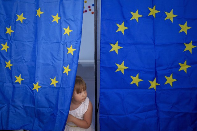 A child peers from a voting cabin during European and local elections in Baleni, Romania, Sunday, June 9, 2024. Voters across the European Union are going to the polls on the final day of voting for the European parliamentary elections to choose their representatives for the next five-year term. (Photo by Andreea Alexandru/AP Photo)