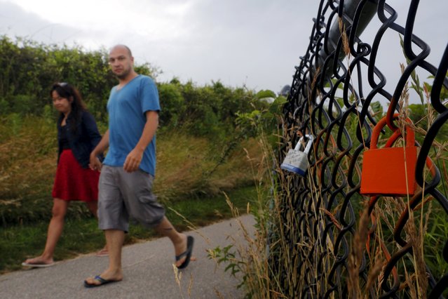 A couple walks past a lock left on a fence along the Cliff Walk in Newport, Rhode Island July 14, 2015. (Photo by Brian Snyder/Reuters)
