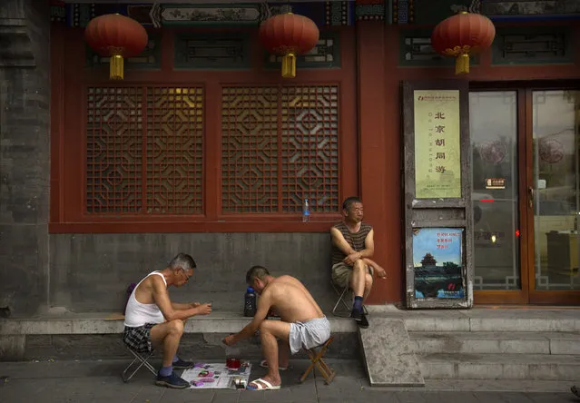 Men play cards on a newspaper as another man sits on a chair outside of an old building in Beijing, Sunday, June 18, 2017. The center of China's capital was once dominated by traditional hutongs, or alleyways, full of historic courtyard homes, but many have been demolished during decades of growth and redevelopment. (Photo by Mark Schiefelbein/AP Photo)