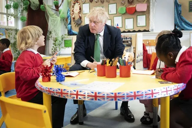 British Prime Minister Boris Johnson sits at a desk with some pupils as he pays a visit to St Mary Cray Primary Academy, in Orpington, England, Monday May 23, 2022 to see how they are delivering tutoring to help children catch up following the pandemic. (Photo by Stefan Rousseau/Pool via AP Photo)
