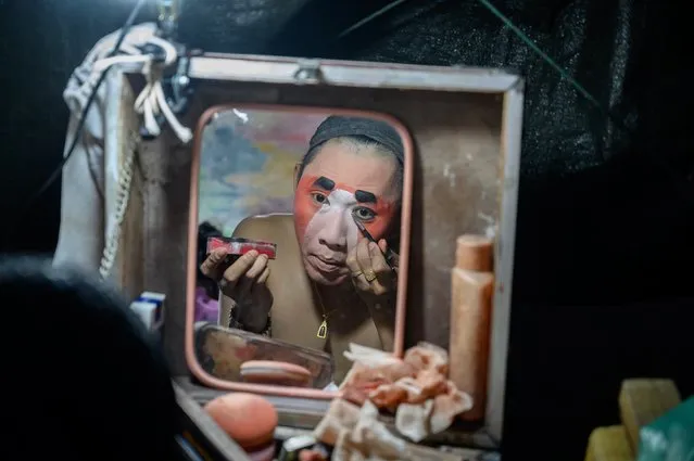 This photograph taken on December 28, 2019 shows a reflection of an actor applying makeup before a Chinese opera performance by Thailand's Sai Bo Hong troupe on a makeshift stage at a street festival in Bangkok. An ancient world of swords, warriors and folklore roars to life on the darkened street, offering a momentary escape from the modern-day bustle of Bangkok's unstoppable development. For centuries, troupes like the Sai Bo Hong Chinese opera have performed throughout Thailand, where 14 percent of the population are ethnic Chinese. (Photo by Mladen Antonov/AFP Photo)