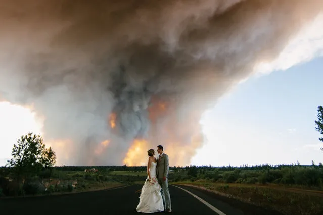 Wedding photographer, Josh Newton, has managed to turn a natural disaster into an amazing photo shoot opportunity. On June 7, 2014 Michael Wolber and April Hartley were getting ready to walk down the aisle in Rock Springs Ranch, Bend, Oregon, USA when firefighters alerted them to nearby wildfires gaining momentum and instructed them to flee to a safer location. Instead of leaving immediately, the wedding coordinator talked the firemen into letting the couple get married if they shortened the ceremony. (Photo by Josh Newton/IMP)