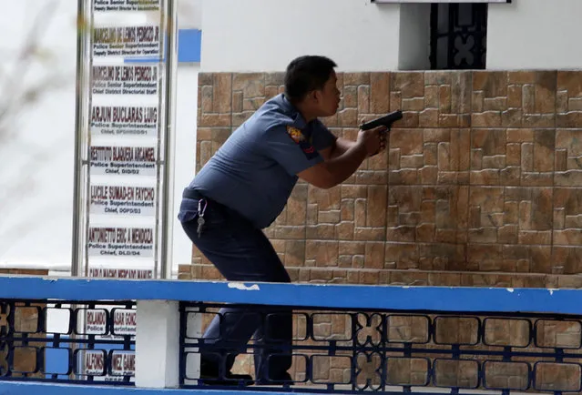A policeman holds his weapon as he takes up a position, after a fellow policeman, who is high on drugs according to a police officer, run berserk at Manila Police Department in Manila, Philippines July 3, 2016. (Photo by Czar Dancel/Reuters)