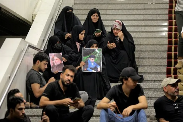 Followers of Shiite cleric Muqtada al-Sadr hold posters with his photo during a sit-in, inside the parliament in Baghdad, Iraq, Monday, August 1, 2022. The political rivals of al-Sadr whose followers stormed the parliament have declared their own counter-protest. The announcement on Monday stirred fear among Iraqis and caused security forces to erect concrete barriers leading to the heavily fortified Green Zone, home of the parliament building. (Photo by Anmar Khalil/AP Photo)