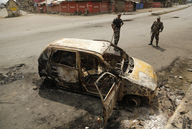 Indian paramilitary soldiers stand near a vehicle of a police officer that was burnt by protestors on Thursday night, on the outskirts of Srinagar, Indian controlled Kashmir, Friday, July 15, 2016. (Photo by Mukhtar Khan/AP Photo)