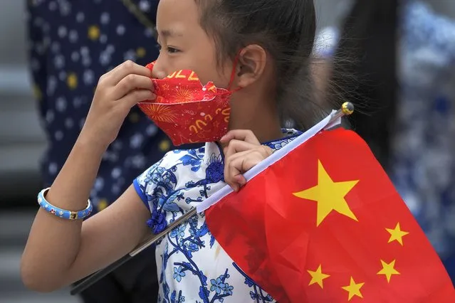 A child holds a national flag while adjusting her face mask on a street in Beijing, Tuesday, August 9, 2022. Chinese authorities have closed Tibet's famed Potala Palace after a minor outbreak of COVID-19 was reported in the Himalayan region. (Photo by Andy Wong/AP Photo)