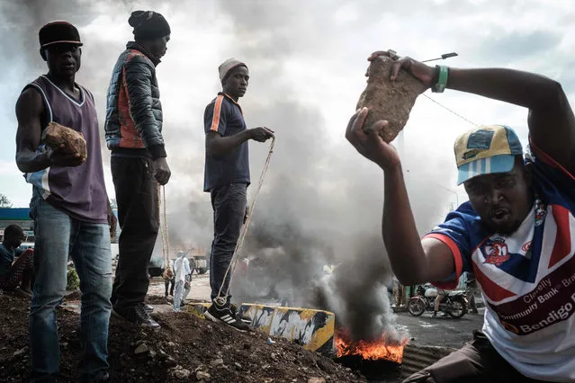 Opposition supporters hold up bricks as they block streets and burn tires during a protest in Kisumu, Kenya, on October 11, 2017. Supporters of Kenya' s opposition leader Raila Odinga took to the streets as poll officials mull their next move after his withdrawal from a presidential election plunged the country into uncharted waters. (Photo by Yasuyoshi Chiba/AFP Photo)