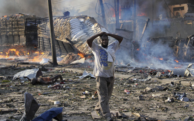 A Somali gestures as he walks past a dead body, left, and destroyed buildings at the scene of a blast in the capital Mogadishu, Somalia Saturday, October 14, 2017. A huge explosion from a truck bomb has killed at least 20 people in Somalia's capital, police said Saturday, as shaken residents called it the most powerful blast they'd heard in years. (Photo by Farah Abdi Warsameh/AP Photo)