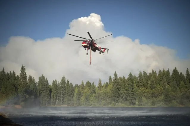 A helicopter draws water from a lake as smoke rises from the King Fire in Pollock Pines, California September 17, 2014. (Photo by Noah Berger/Reuters)