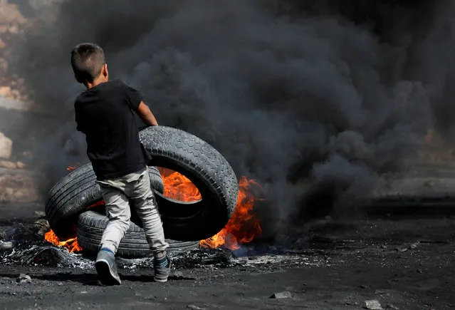 A Palestinian boy puts a tyre on fire during clashes with Israeli troops near the Jewish settlement of Qadomem, in the West Bank village of Kofr Qadom, near Nablus, October 20, 2017. (Photo by Mohamad Torokman/Reuters)