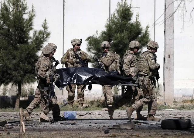 U.S. troops carry the dead body of a member of an international troop at the site of a suicide attack in Kabul September 16, 2014. A huge explosion rattled windows in Afghanistan's capital early on Tuesday, sending a plume of white smoke rising above eastern Kabul. The bomb attack near the U.S. embassy killed four troops from the NATO-led international military force, the coalition said in a statement. At least five were wounded in the blast, which was claimed by the Taliban. (Photo by Mohammad Ismail/Reuters)