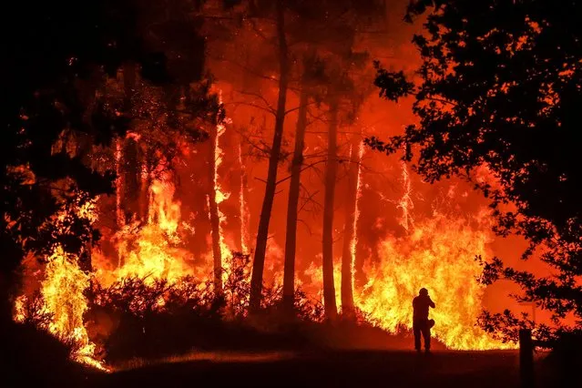 A silhouette is seen in front of flames at a wildfire near Belin-Beliet, southwestern France, overnight on August 11, 2022. French officials warned that flare-ups could cause a massive wildfire to further spread in the country's parched southwest, where fresh blazes have already blackened swathes of land this week. Prime Minister is expected to meet with authorities battling the Landiras blaze south of Bordeaux, and further reinforcements are expected for the 1,100 firefighters on site, the prefecture of the Gironde department said. (Photo by Thibaud Moritz/AFP Photo)