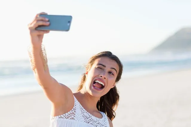 Playful young woman taking selfie with smartphone on the beach. (Photo by Letizia Le Fur/Getty Images)