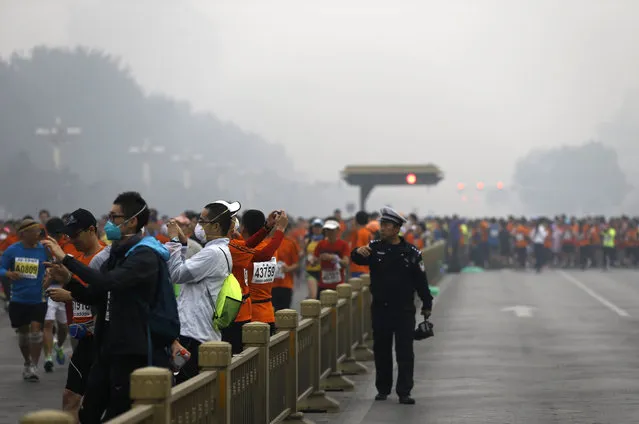A traffic policeman asks runners, some are wearing masks to protect themselves from pollutants, to move along as others jog past Chang'an Avenue near Tiananmen Square shrouded in haze at the start of 2014 Beijing International Marathon in Beijing, China Sunday, October 19, 2014. (Photo by Andy Wong/AP Photo)