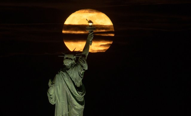 A 99 percent illuminated Pink Moon rises behind the Statue of Liberty in New York City one day after being full on April 13, 2025, as seen from Jersey City, New Jersey. (Photo by Gary Hershorn/Getty Images)