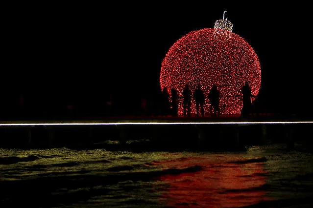People are silhouetted on a pedestrian dock decorated with an illuminated Christmas ornament in the southern coastal city of Larnaca on the eastern Mediterranean island of Cyprus, Sunday, December 17, 2017. (Photo by Petros Karadjias/AP Photo)